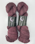 Two skeins of hand-dyed purple yarn with labels on a white background