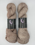 Three skeins of hand-dyed tan yarn with labels on a white background