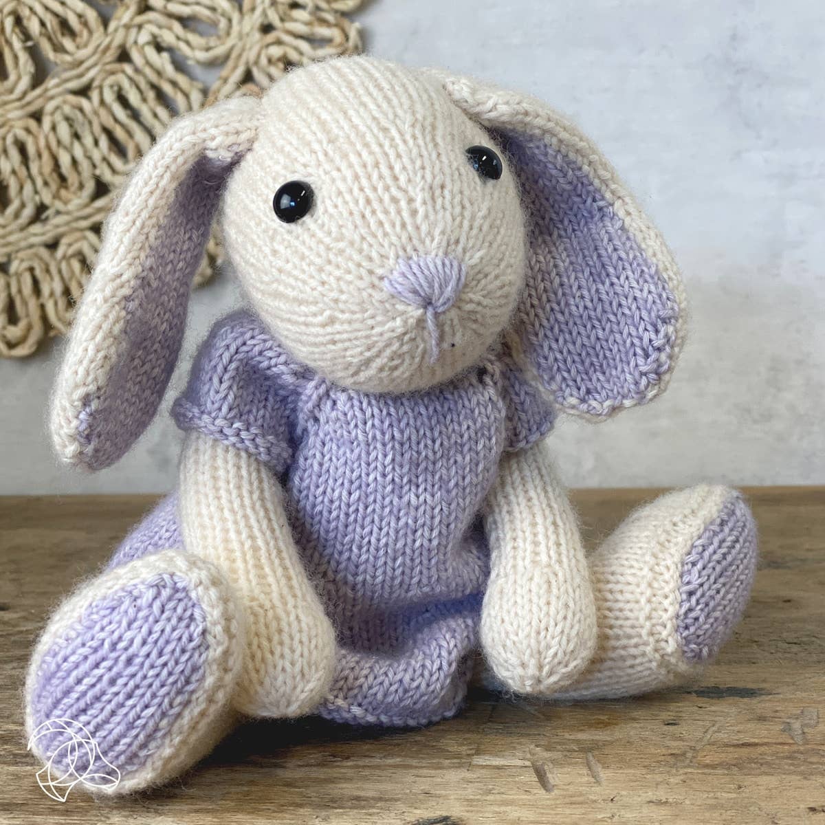 Knitted bunny toy with purple accents and dress on a wooden surface