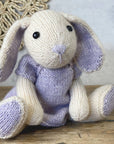 Knitted bunny toy with purple accents and dress on a wooden surface