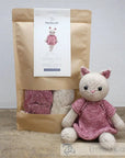 Knitted cat toy in a pink dress next to a package of yarn on a wooden surface.