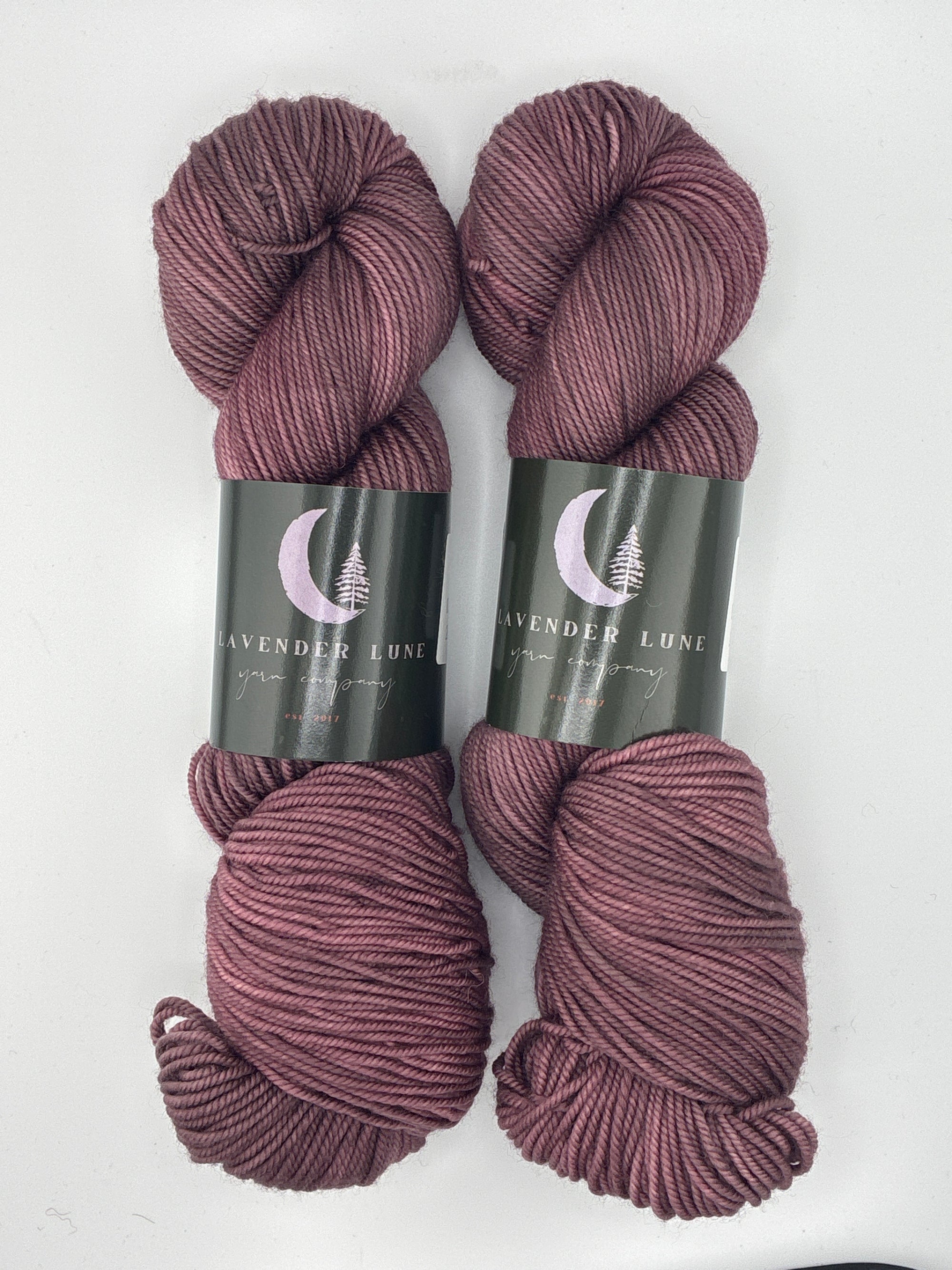 Two skeins of hand-dyed purple yarn with labels on a white background