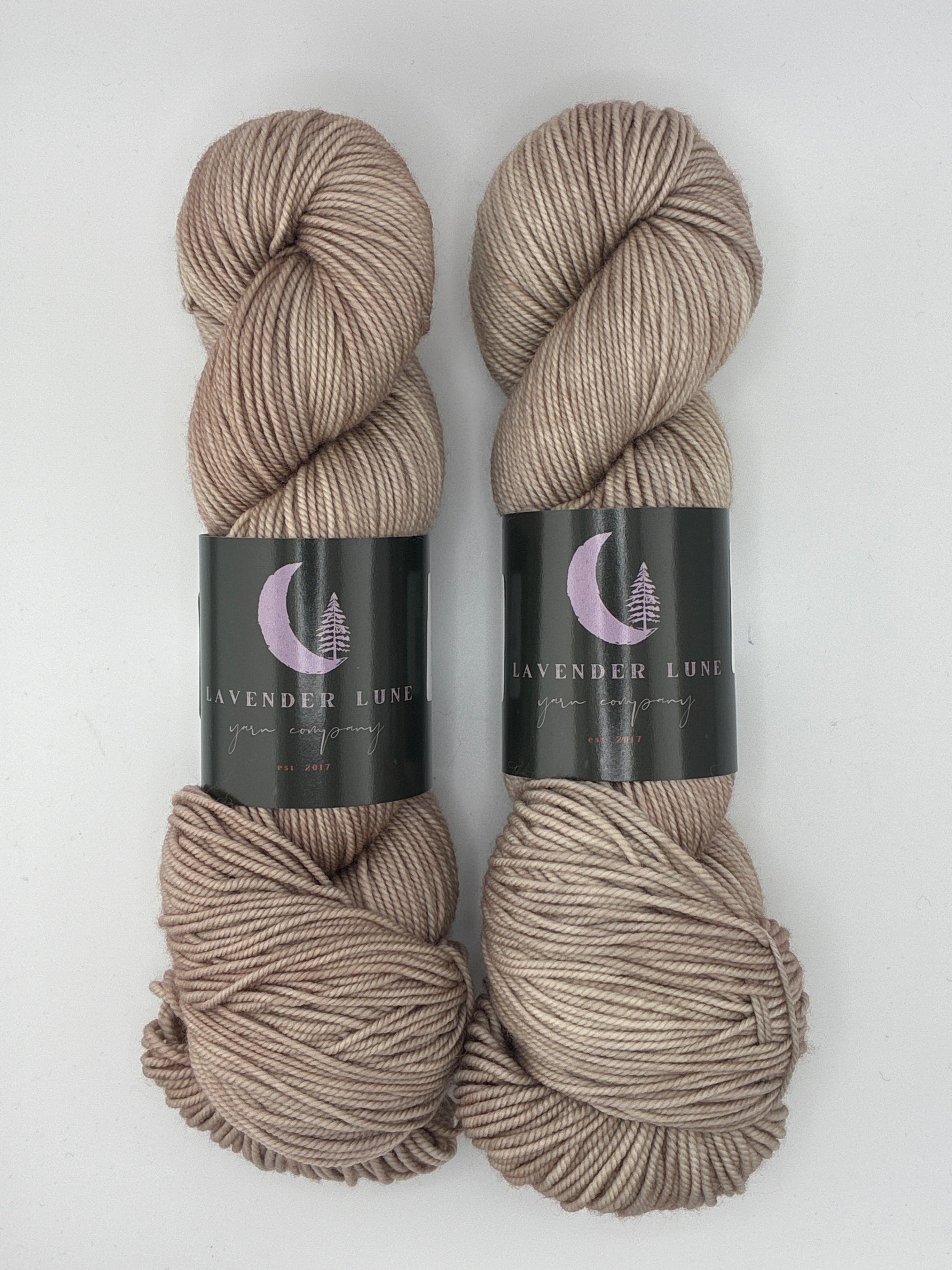 Three skeins of hand-dyed tan yarn with labels on a white background