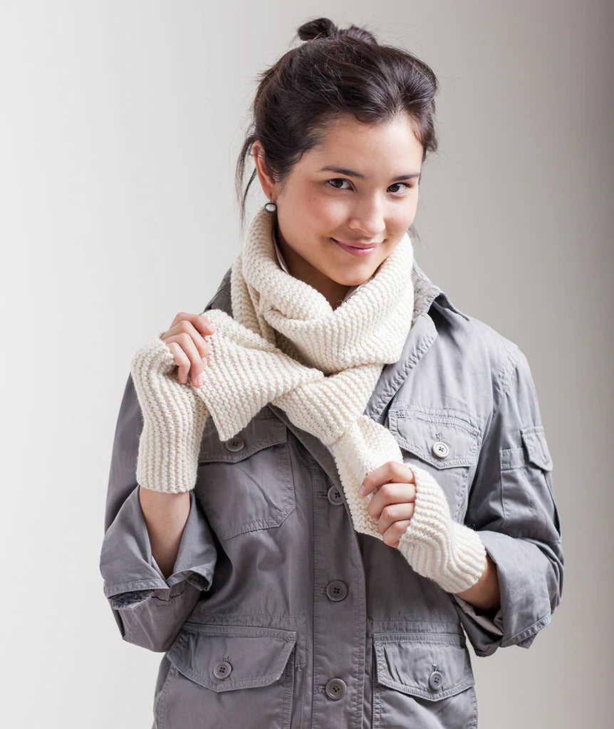 Woman wearing a white knitted scarf and gray jacket against a plain background