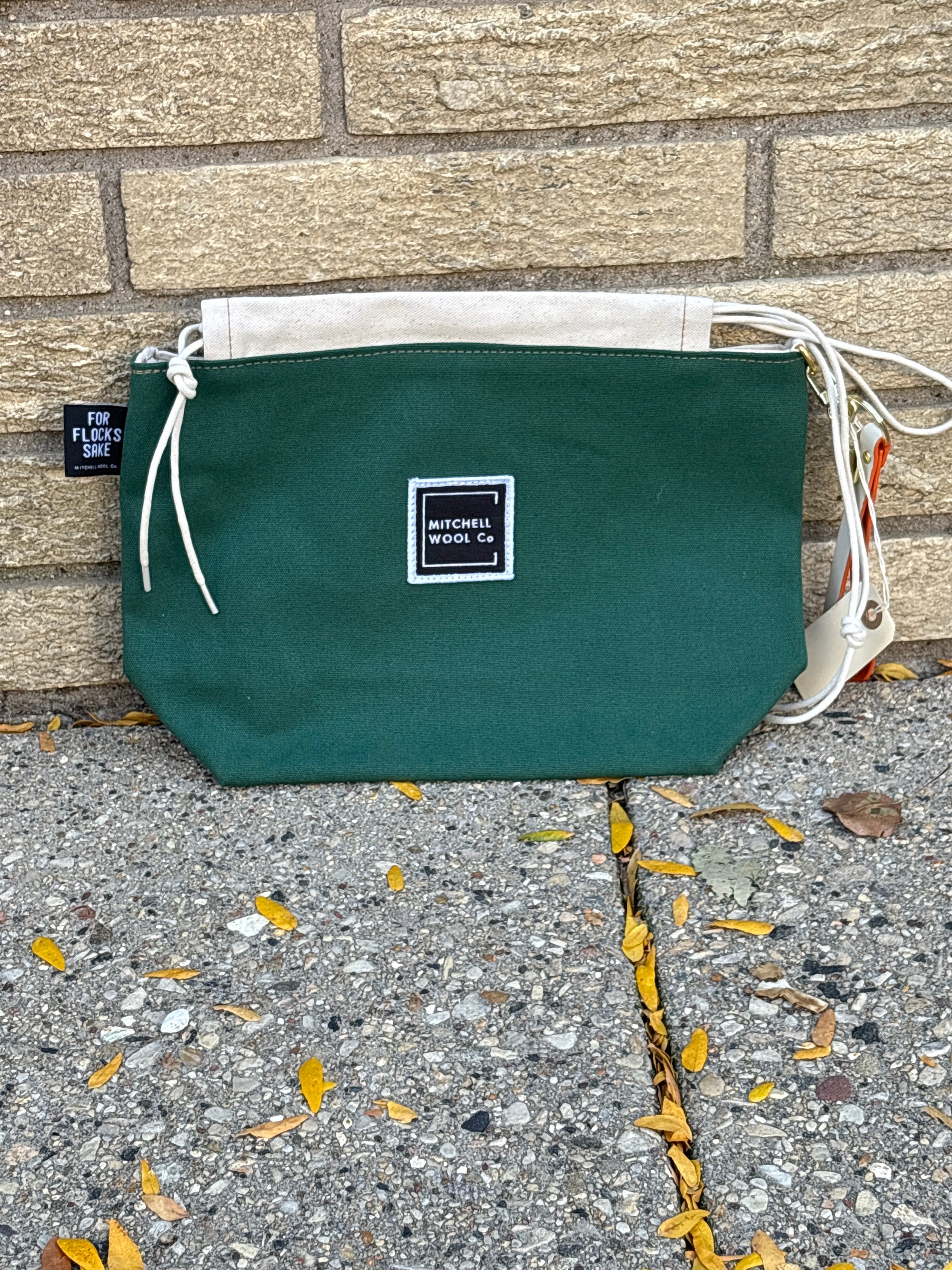 Green pouch with a Mitchell Wool brand label on a concrete surface with leaves