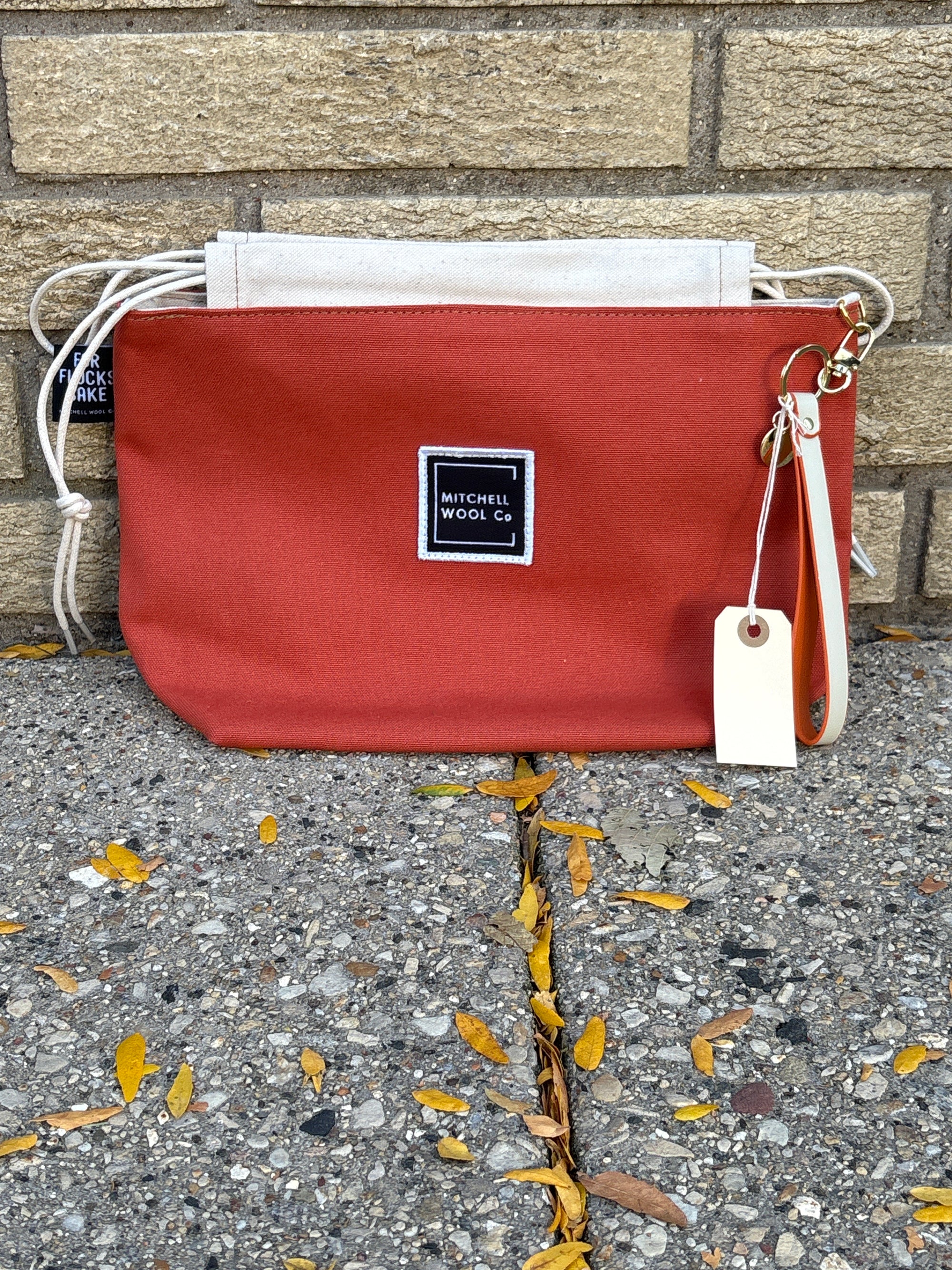 Terracotta pouch with a white strap on a concrete surface with leaves