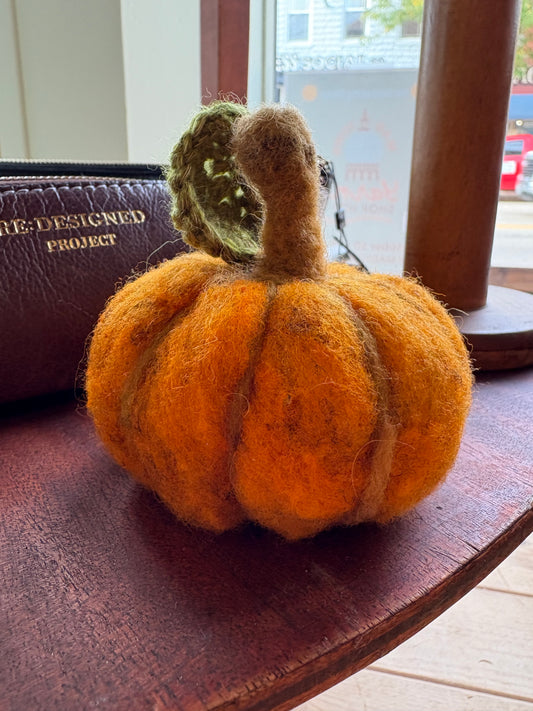 Felted pumpkin on a wooden surface with a blurred background
