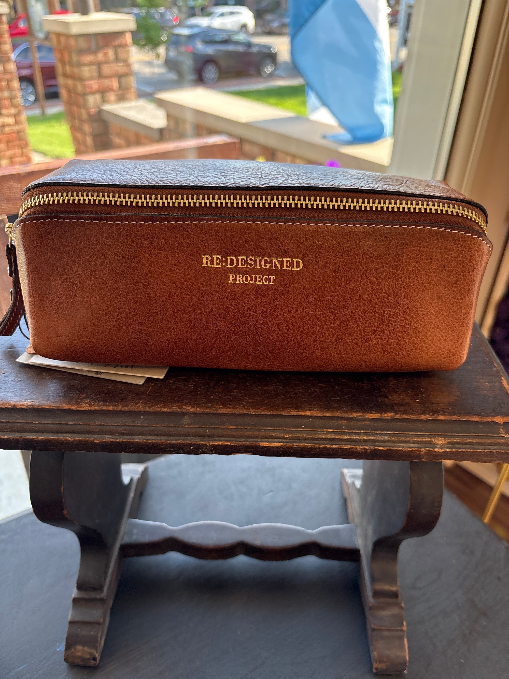 Brown leather knitting project bag with 'RE-DESIGNED PROJECT' branding on a wooden surface.