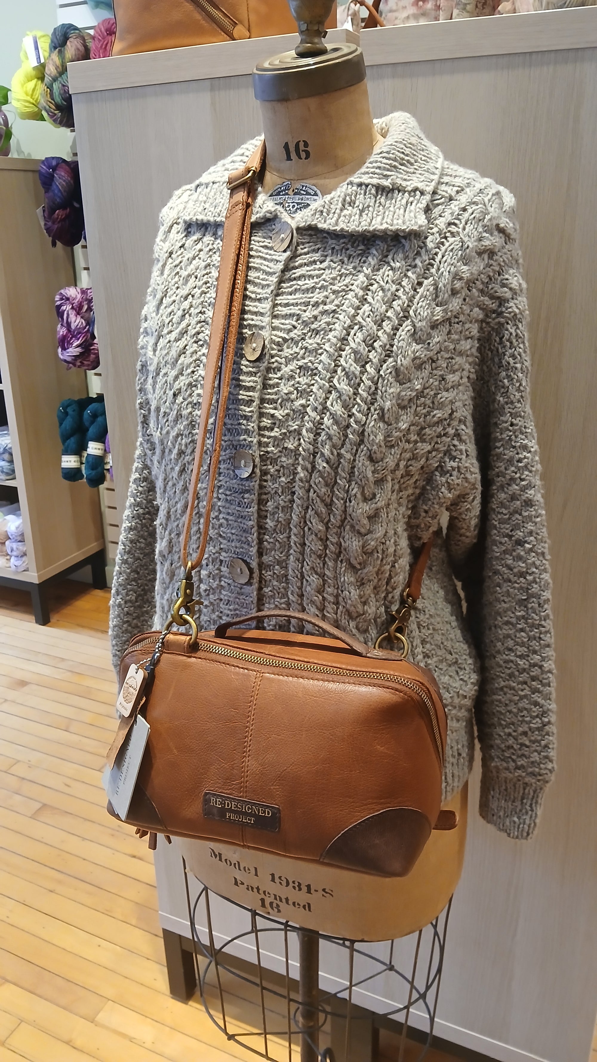 Mannequin wearing a textured sweater with a brown leather Re:Designed project bag.