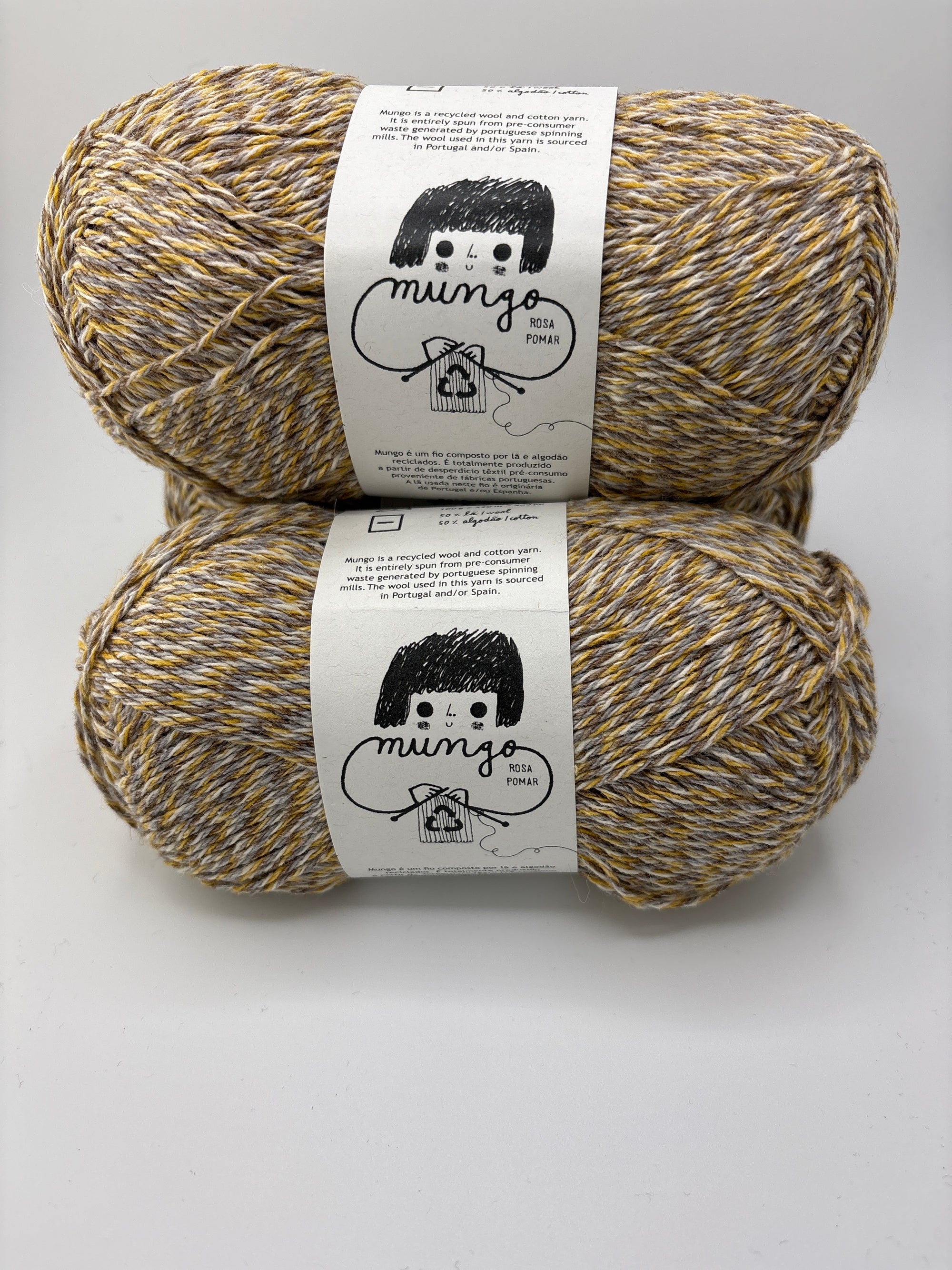 Two skeins of tan, yellow and gray marled yarn with labels on a white background
