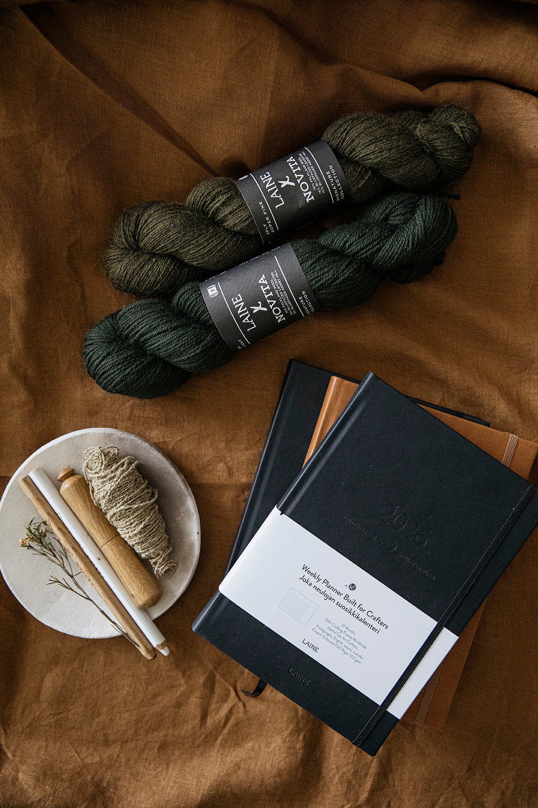 Two skeins of yarn and a weekly knitting planner on a brown fabric background